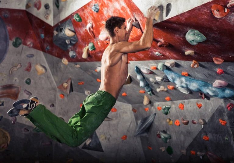 Muscular man practicing rock-climbing on a rock wall indoors